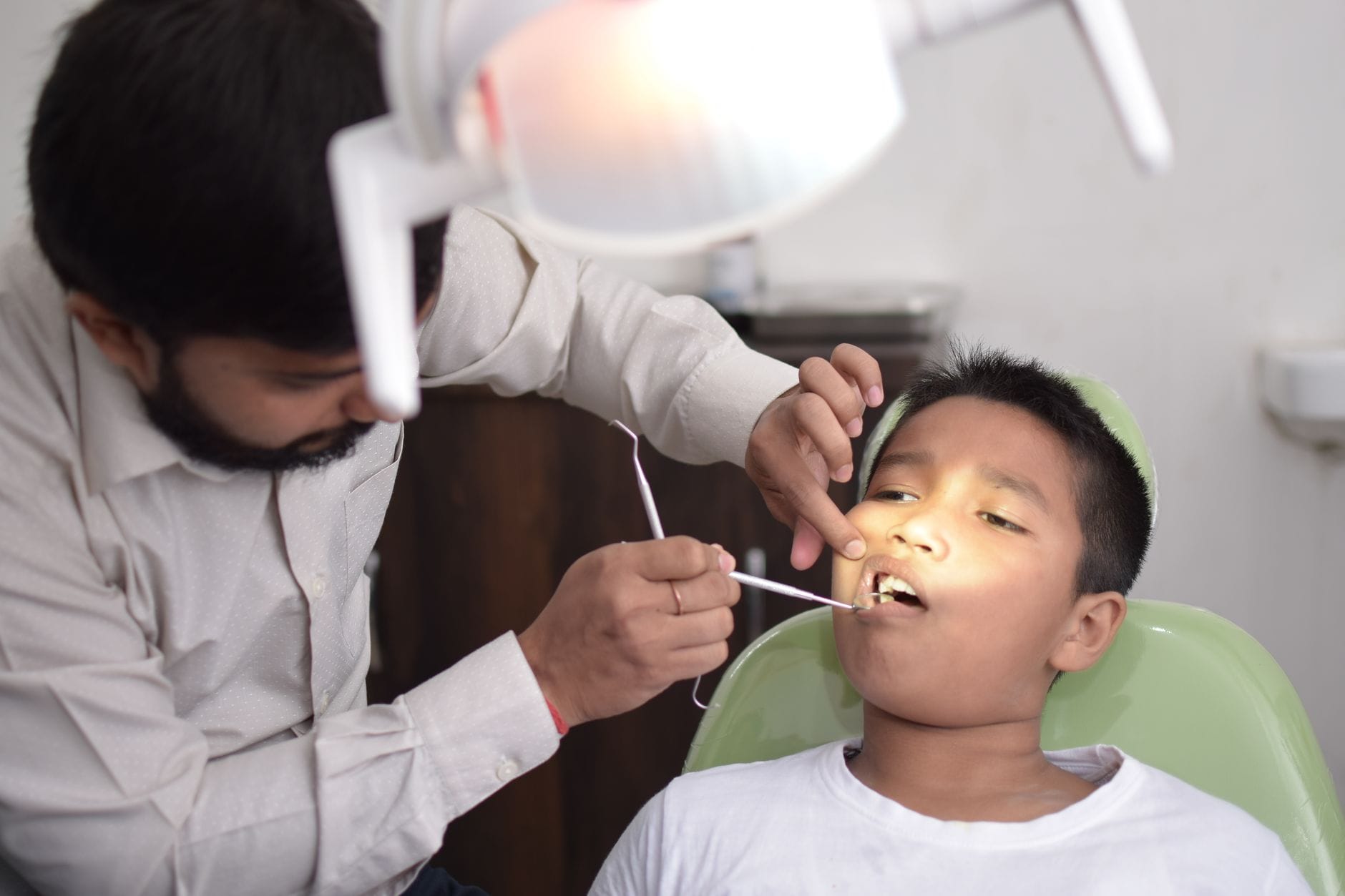 Dentist leaning over a young patient in a dental chair, using tools to examine the mouth during a checkup in a clinic.
