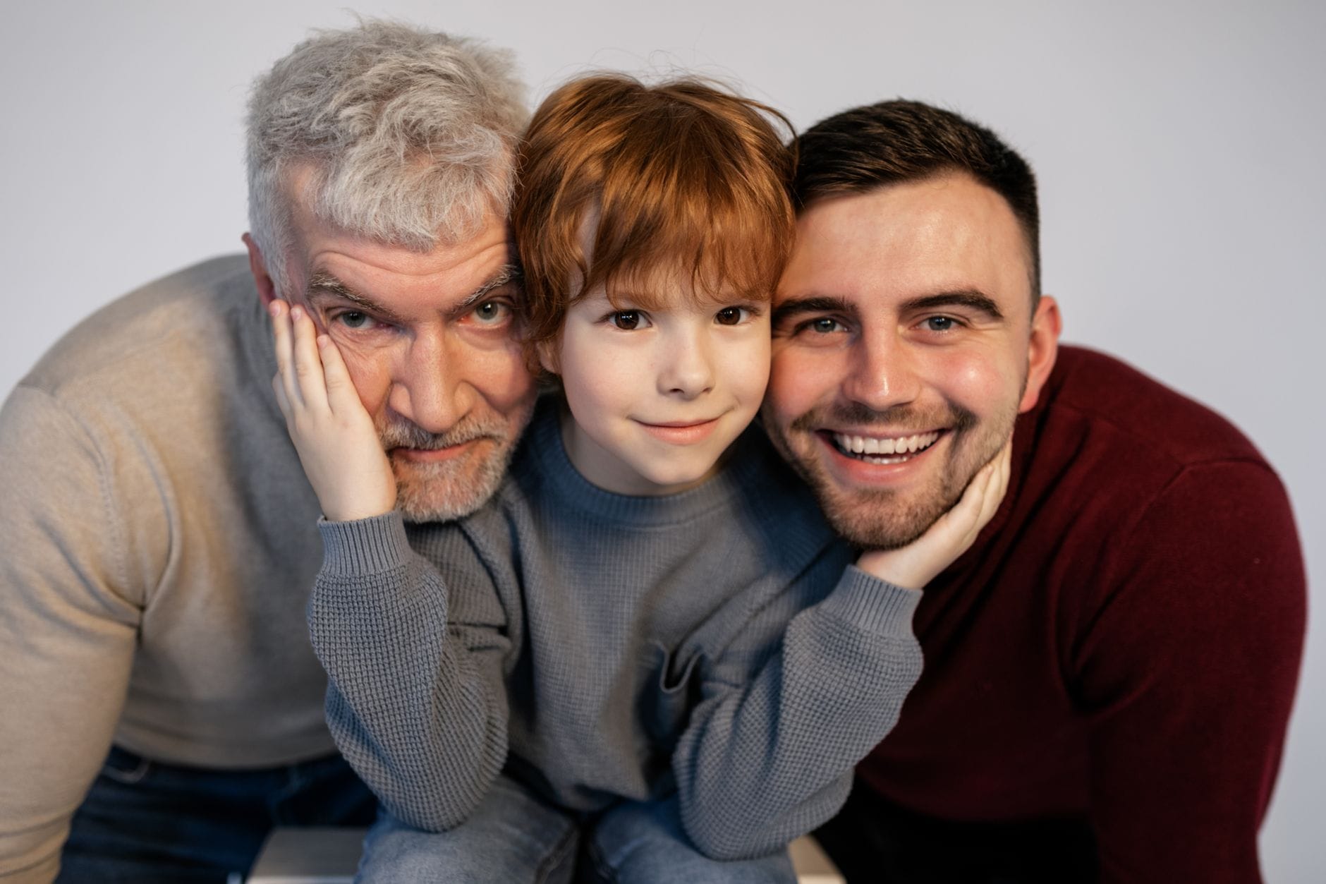 Grandfather, father, and son sit close together, smiling at the camera.